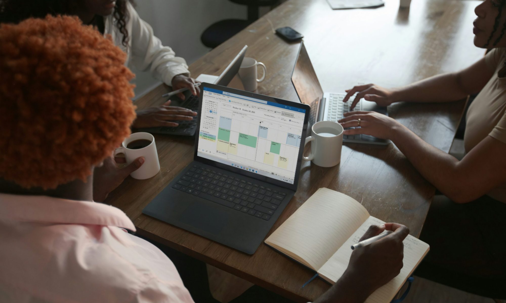 Three people in a meeting at a table discussing schedule on their Microsoft laptop