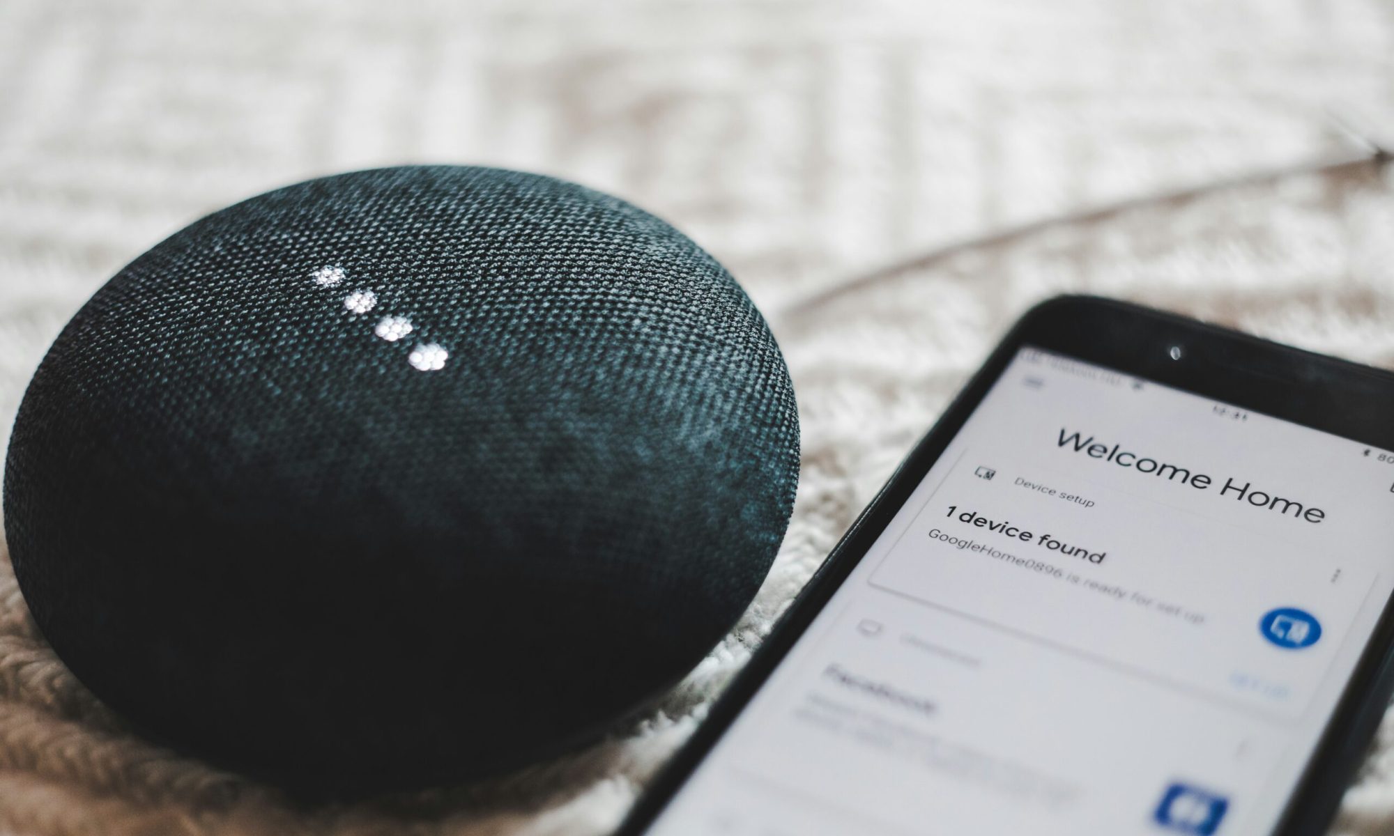 turned-on charcoal Google Home Mini and smartphone